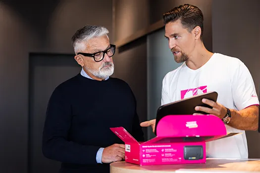 Junger Mann erklärt älterem Kunden Tablet neben pinker Produktbox im Laden